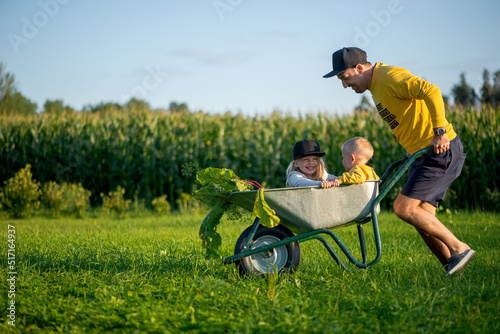 Foto Happy father and his children playing with a wheelbarrow on a sunny autumn day