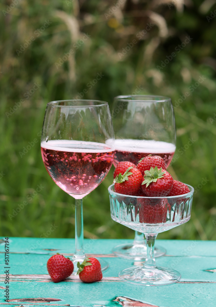Two glasses of rose sparkling wine and strawberry on a table. Romantic picnic outdoors. Close up photo of glass tableware. Summer drinks and food. Two glasses of rose sparkling wine and strawberry on a table. Romantic picnic outdoors. Close up photo of glass tableware. Summer drinks and food.
