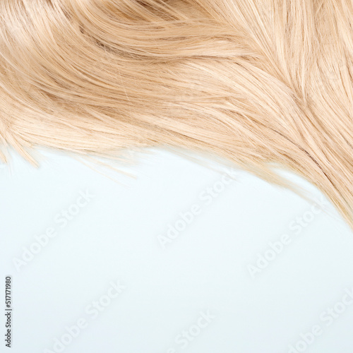 Close-up of a straight shiny blond hair. Hair care and styling concept. Abstract background for hairdresser business. Light blond wig on a light blue. Daily hair beauty routine.