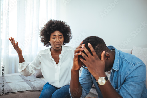 Emotional annoyed stressed couple sitting on couch, arguing at home. Angry irritated nervous woman man shouting at each other photo