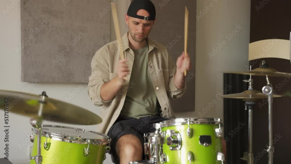 Young man enthusiastically practices playing drums in specifically equipped music studio. Man hits cymbals and drums beating precise rhythm