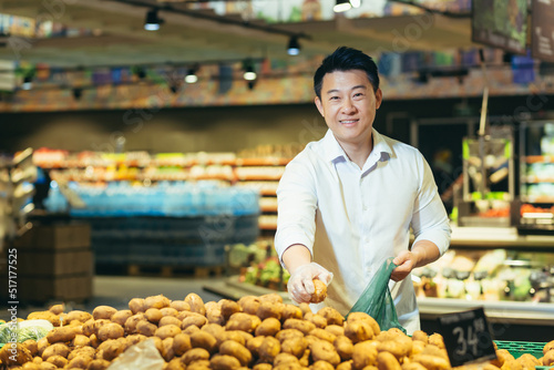 Portrait of an Asian shopper in the grocery department of a supermarket, a man chooses vegetables and buys potatoes, smiling and looking at the camera