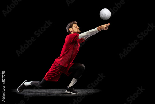 Portrait of young man  volleyball player in motion  training  playing isolated over black studio background. Ball serving