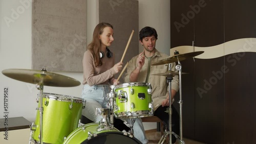 Young woman attends drum classes and music tutor teaches lady basics of playing drums. Girl plays green colored drums in specially equipped music studio photo