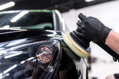 Employee of a car wash or a car detailing studio polishes the car paint with an electric polisher