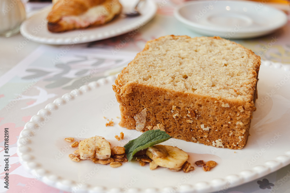 Trozo de budín servido en mesa con decoración de bananas y menta. Merienda.