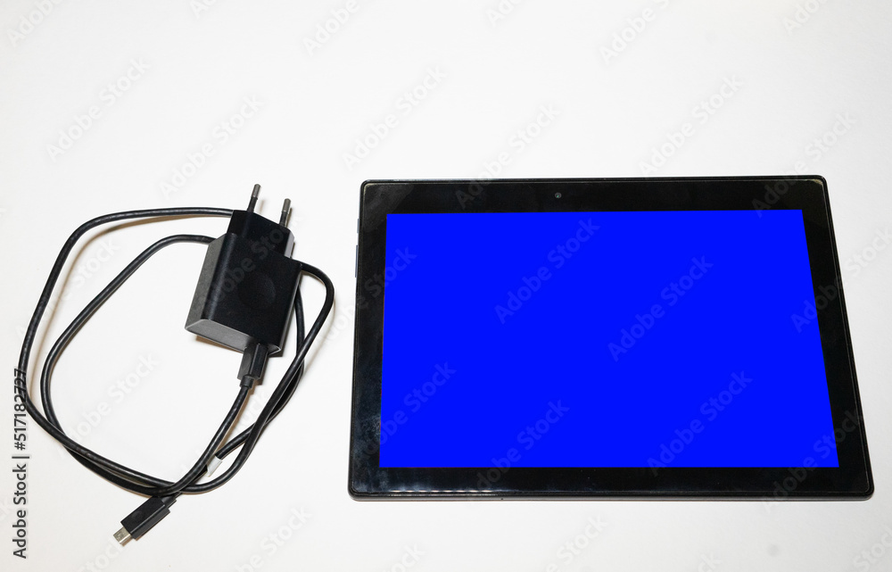 A black tablet with a blue screen and a charger on a white background A black tablet with a blue screen and a charger on a white background