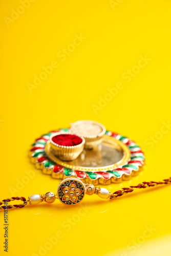 Indian festival raksha bandhan: puja thali and rakhi or wrist band on yellow background.