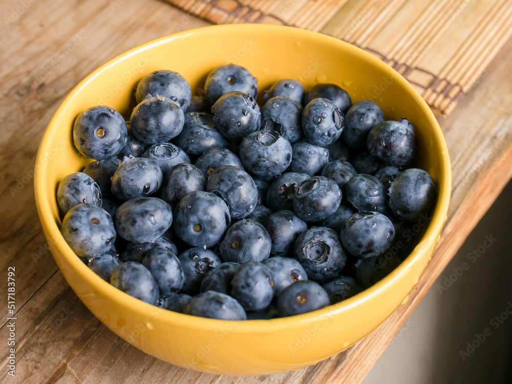 Washed blueberries (Vaccinium uliginosum) in a yellow bowl on a wooden table Washed blueberries (Vaccinium uliginosum) in a yellow bowl on a wooden table
