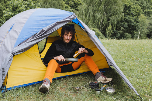 Camping food, a guy sitting in a tent eating breakfast from a bowl, a tourist camp, an overnight stay in nature, a curly hipster tourist dining in the woods, a trip