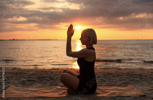 yoga, mindfulness and meditation concept - woman meditating in easy pose on beach over sunset over sunset