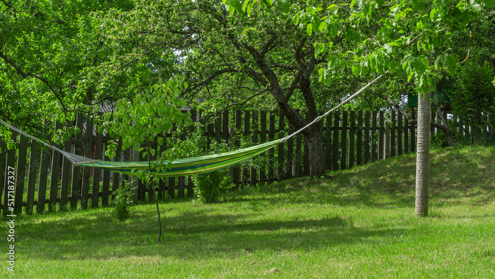 Summer garden with hanging hammock for relaxation. Hammock in backyard on the fence background. Summer garden with hanging hammock for relaxation. Hammock in backyard on the fence background.
