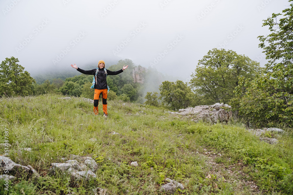 A happy tourist guy with a backpack spread his arms to the sides, the delight and happiness of the beauty of nature, the morning fog in the mountains.
