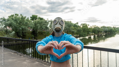 A girl in a gas mask with her hands shows a heart symbol. Alienation in the city. Fashion, ecology and loneliness concepts.