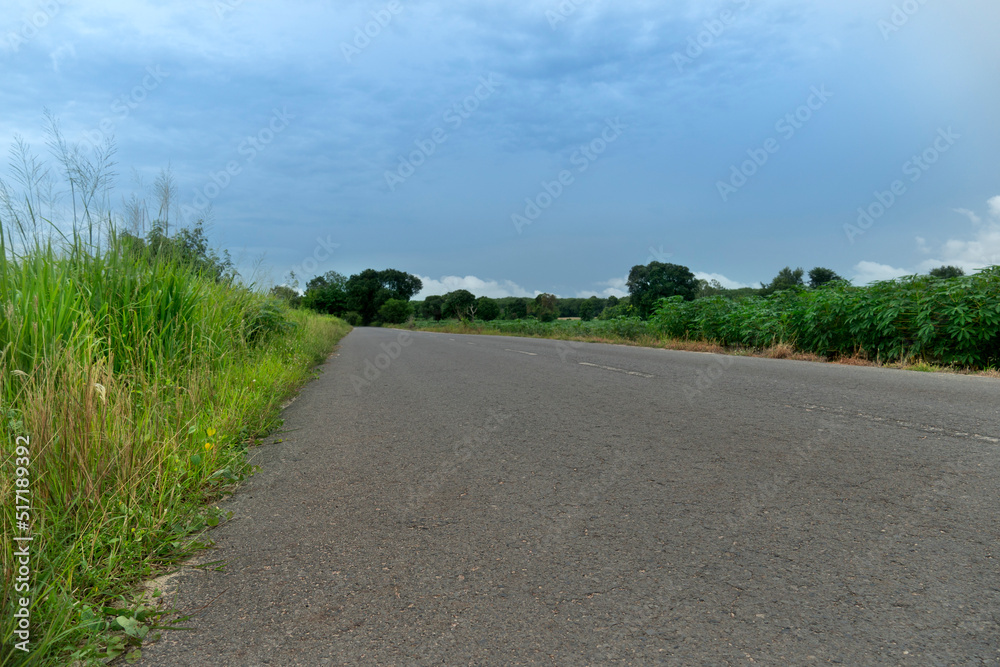 Country road in Thailand. Beside with green grass. empty asphalt road path. under the gloomy sky.