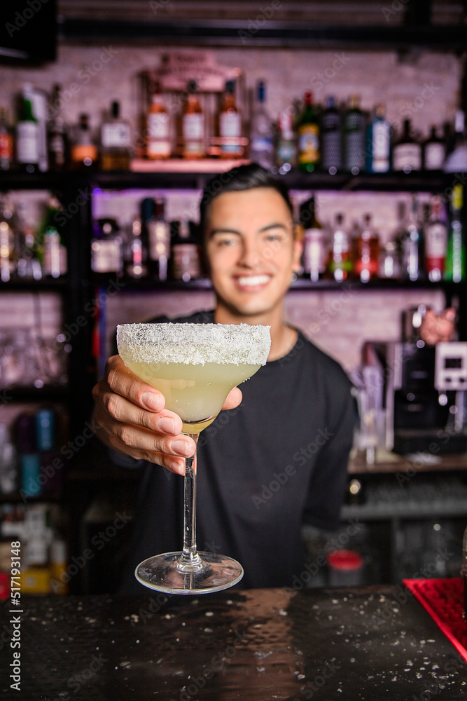 unfocused young waiter shows a margarita cocktail on camera in the foreground