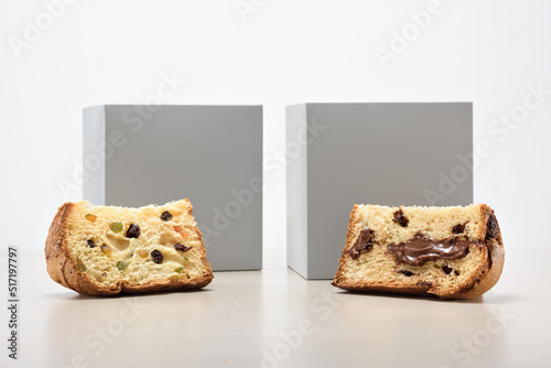 Two slices of chocolate and dried fruit filled panettone, with two gray boxes behind, isolated on white