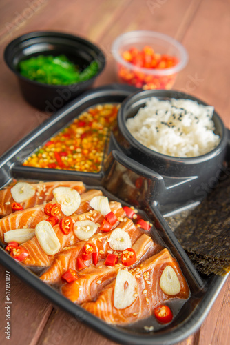 Salmon pickled in soy sauce or shoyu sauce and sprinkled with chili and sliced garlic. with spicy sauce Seaweed and Japanese rice are side dishes on a brown wooden table.