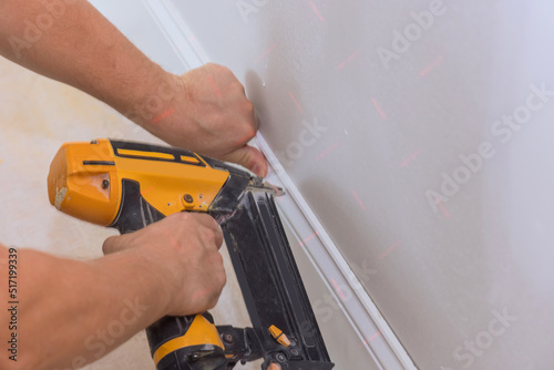 Carpenter using a brad nail gun to nailing base molding trim for works new home