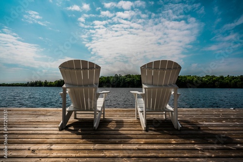 Fotografie Wooden pier with white chairs facing the lake and green forest