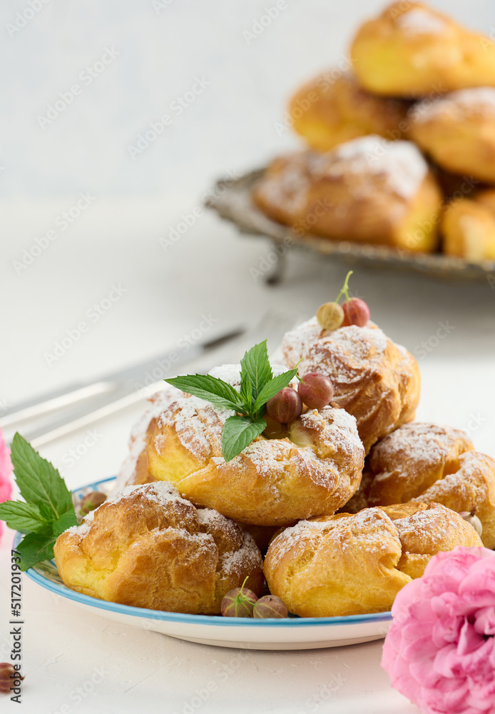 Baked eclairs with custard cream on a metal round plate sprinkled with powdered sugar Baked eclairs with custard cream on a metal round plate sprinkled with powdered sugar
