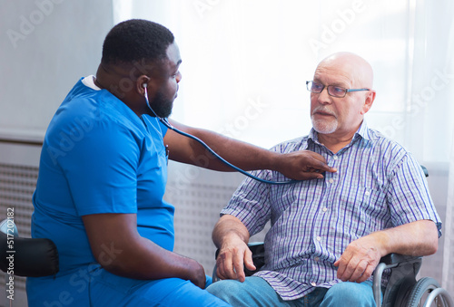 Professional doctor helps an elderly man with chronic diseases. Therapist and patient in home interior. Health care and medicine concept.