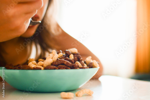 Close up view caucasian boy sit to eat cereals in kitchen on white table. Food in focus blurry people intentional bright background