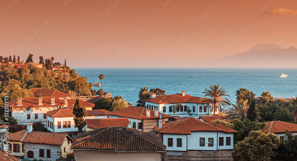 Panoramic scenic rooftop cityscape view of mediterranean resort old town and blue sea in the background at golden summer sunset time