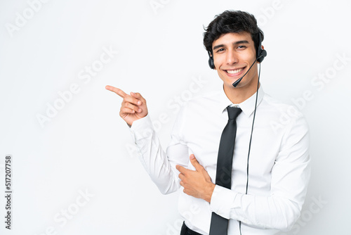 Telemarketer man working with a headset isolated on white background pointing finger to the side