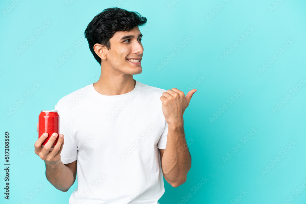 Young Argentinian man holding a refreshment isolated on blue background pointing to the side to present a product Young Argentinian man holding a refreshment isolated on blue background pointing to the side to present a product