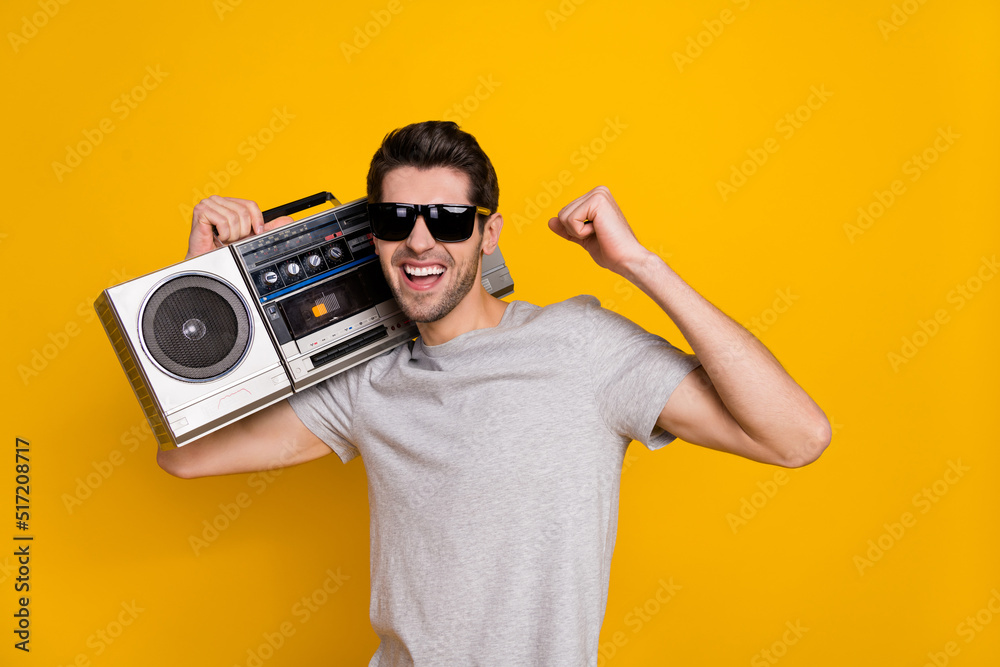 Photo of cute brunet young guy hold boombox wear t-shirt glasses isolated on yellow background Photo of cute brunet young guy hold boombox wear t-shirt glasses isolated on yellow background
