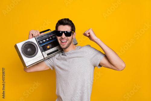 Photo of cute brunet young guy hold boombox wear t-shirt glasses isolated on yellow background