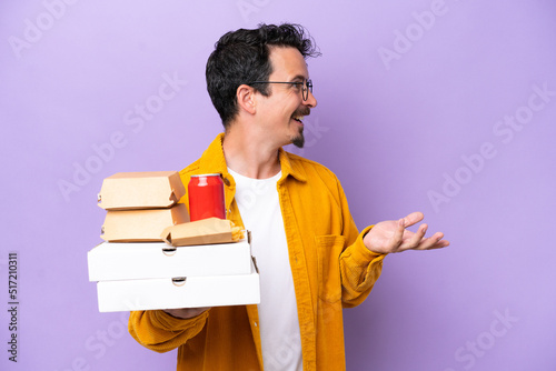 Young caucasian man holding fast food isolated on purple background with surprise expression while looking side