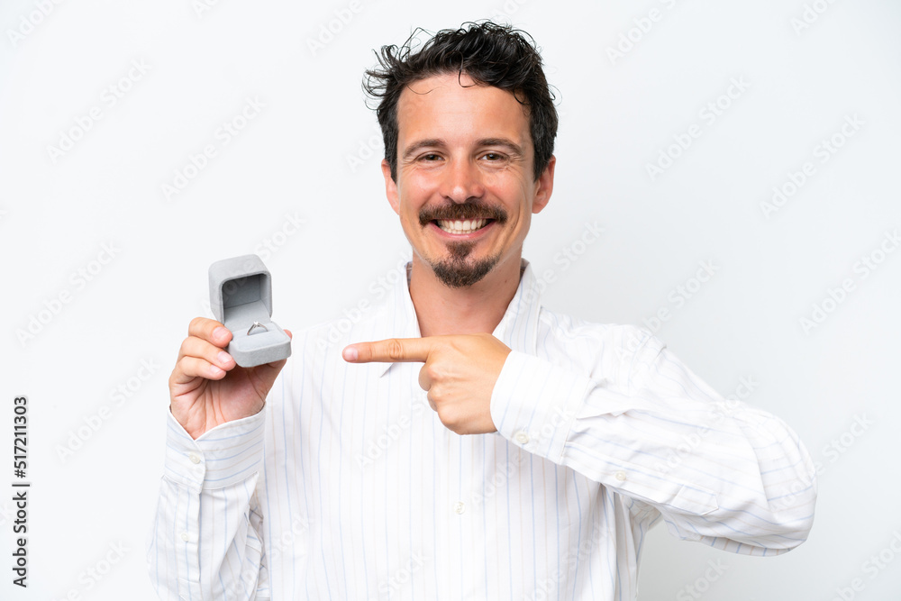 Young man holding a engagement ring isolated on white background and pointing it Young man holding a engagement ring isolated on white background and pointing it
