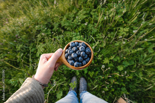 Ripe  juicy blueberries  in traditional wooden Sami Cup (kuksa) in hand on a background of green grass. Vegan, healthy, lifestyle concept. Freshly picked blueberries.