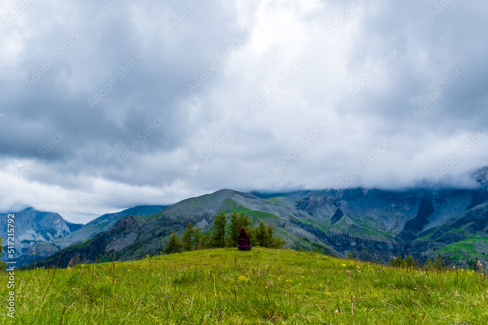 A wide angle shot of a young female hiker on a break during a hike on a cloudy summer day in the French Alps (Valberg, Alpes-Maritimes, France) A wide angle shot of a young female hiker on a break during a hike on a cloudy summer day in the French Alps (Valberg, Alpes-Maritimes, France)