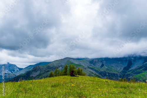 A wide angle shot of a young female hiker on a break during a hike on a cloudy summer day in the French Alps (Valberg, Alpes-Maritimes, France) © k.dei