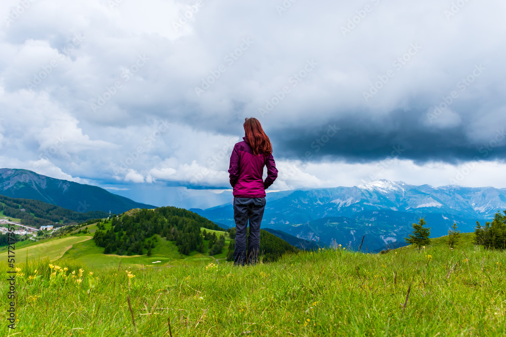 A wide angle shot of a young female hiker on a break during a hike on a cloudy summer day in the French Alps (Valberg, Alpes-Maritimes, France)
