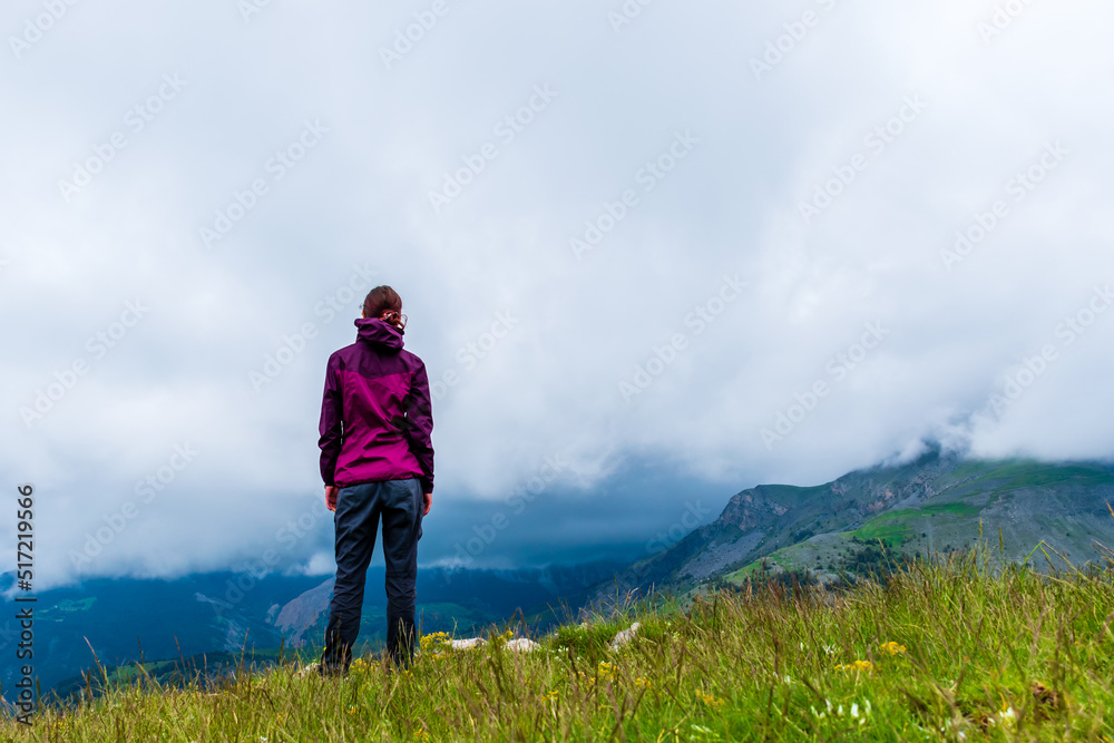 A wide angle shot of a young female hiker on a break during a hike on a cloudy summer day in the French Alps (Valberg, Alpes-Maritimes, France)