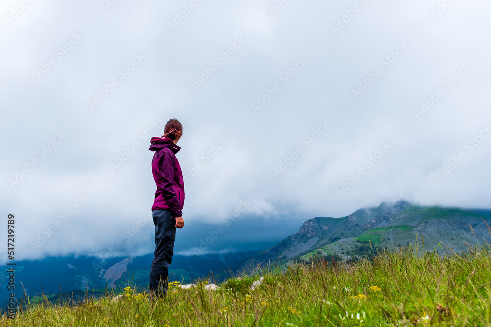 A wide angle shot of a young female hiker on a break during a hike on a cloudy summer day in the French Alps (Valberg, Alpes-Maritimes, France)