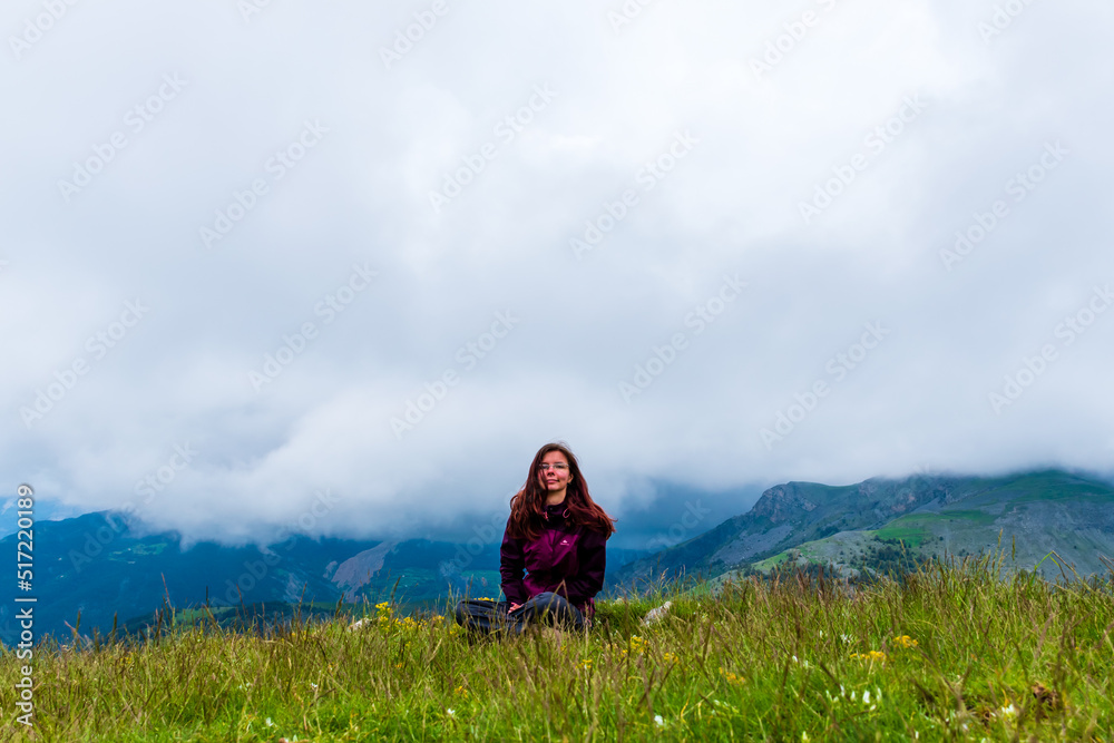 A wide angle shot of a young female hiker on a break during a hike on a cloudy summer day in the French Alps (Valberg, Alpes-Maritimes, France) A wide angle shot of a young female hiker on a break during a hike on a cloudy summer day in the French Alps (Valberg, Alpes-Maritimes, France)