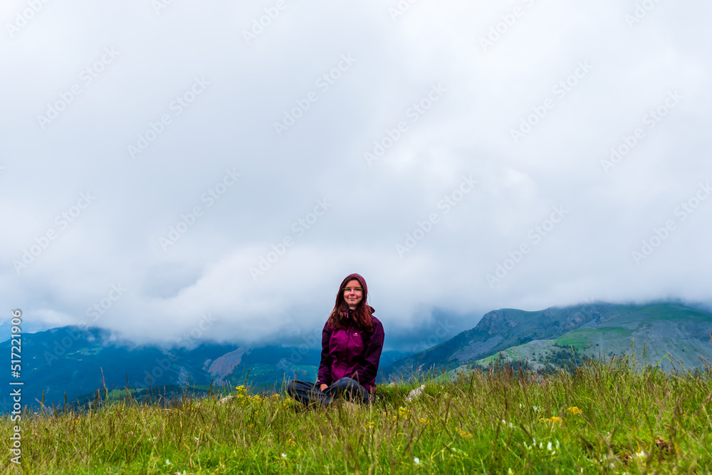 A wide angle shot of a young female hiker on a break during a hike on a cloudy summer day in the French Alps (Valberg, Alpes-Maritimes, France)