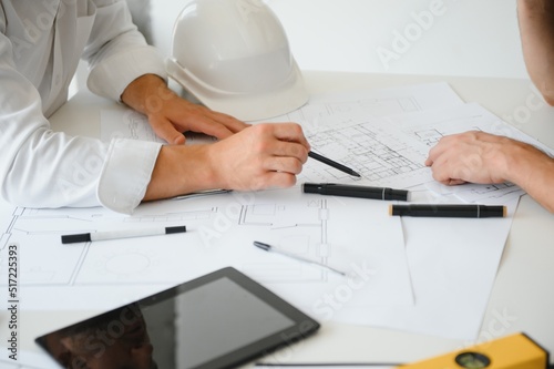 Two engineering working together and using digital tablet looking blueprint and analysis with architectural plan on desk