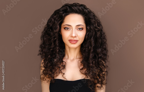 Curly hair woman. Beauty portrait of young beautiful brunette model with wavy healthy hair against brown background.