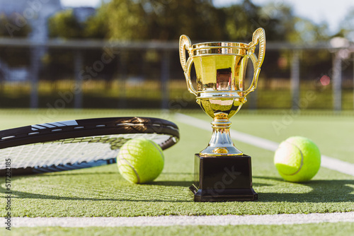Golden champion cup with tennis racket and balls on the playing court. Sport award. Victory concept