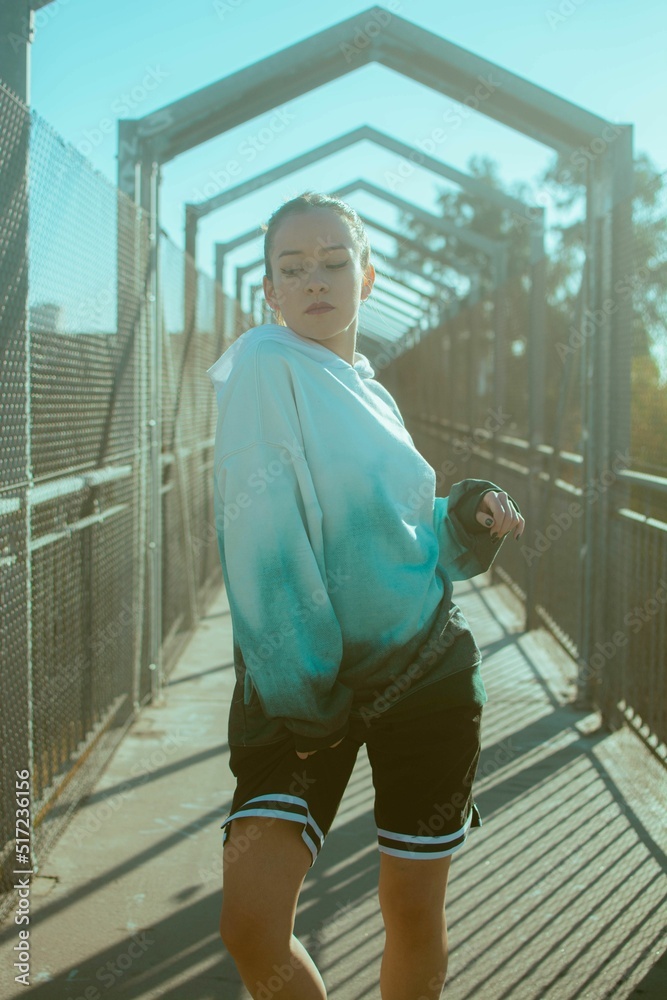 Girl in hoodie and shorts poses in front of camera on pedestrian