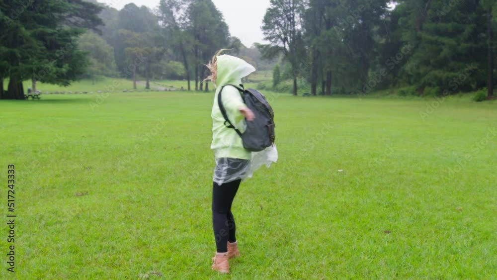 Happy cute smiling young woman with raised hands in raincoat enjoying rain and having fun under rainfall. Tourist playing with drops rain in forest. Happy girl summer autumn childhood dream concept 4K Happy cute smiling young woman with raised hands in raincoat enjoying rain and having fun under rainfall. Tourist playing with drops rain in forest. Happy girl summer autumn childhood dream concept 4K