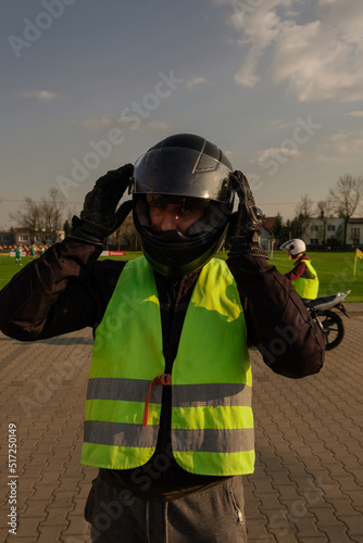 Заголовок Motorcyclist in a driving lesson. Lessons in auto and motorcycle school. A student in a special uniform drives a motorcycle. Summer training on a moped. Student and teacher. 