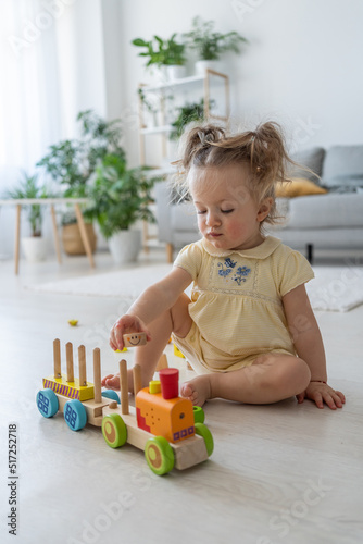 Active girl. Vertical shot of the baby playing with wooden developing toys alone at home. Eco-friendly wooden toys for children. Happy childhood concept
