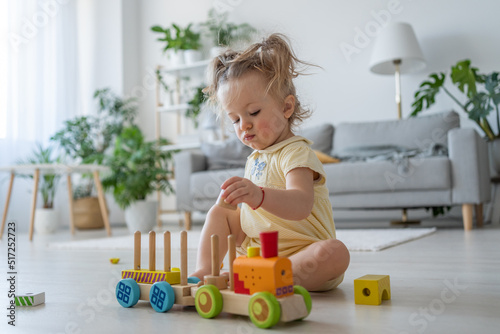 Full length view of the cute little girl playing with colourful wooden toys on floor at home. Toddler kid play attentively. Educational toys for preschool and kindergarten child